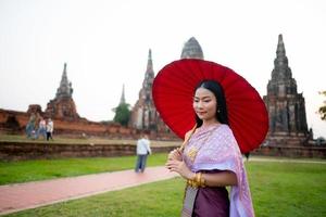 magnifique thaïlandais fille dans traditionnel robe costume rouge parapluie comme thaïlandais temple où est le Publique lieu, thaïlandais femme dans traditionnel costume de Thaïlande. photo