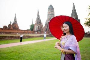 magnifique thaïlandais fille dans traditionnel robe costume rouge parapluie comme thaïlandais temple où est le Publique lieu, thaïlandais femme dans traditionnel costume de Thaïlande. photo