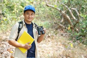 asiatique homme explorateur porte bleu casquette, détient binoculaire dans forêt à enquête botanique les plantes et créatures faune. concept, la nature exploration. écologie et environnement. photo