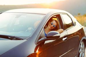 souriant femme conduite une voiture à le coucher du soleil photo