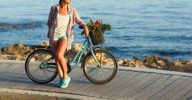 insouciant femme avec vélo équitation sur une en bois chemin à le mer, ayant amusement et souriant photo