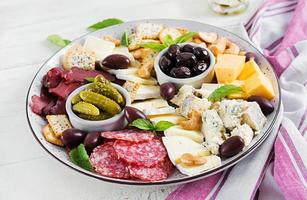 antipasto plat avec basturma, salami, bleu fromage, des noisettes, cornichons et Olives sur une blanc en bois Contexte. photo