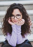 magnifique Jeune femme avec brunette frisé cheveux, portrait dans œil des lunettes profiter le Soleil dans le ville. photo