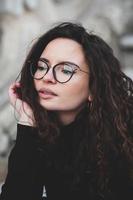 magnifique Jeune femme avec brunette frisé cheveux, portrait dans œil des lunettes profiter le Soleil dans le ville. photo