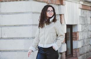 magnifique Jeune femme avec brunette frisé cheveux, portrait dans œil des lunettes profiter le Soleil dans le ville. photo