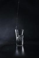 une courant de l'eau verse dans une verre contre une noir Contexte. l'eau éclaboussure. proche en haut photo