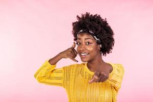 Jeune magnifique femme Faire parlant sur le Téléphone geste et montrer du doigt à toi. africain américain femme portant décontractée vêtements, souriant et à la recherche à caméra photo