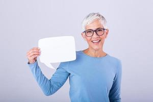 portrait de une un excité mature gris cheveux femme montrant Vide discours bulle isolé plus de gris Contexte. Sénior femme en portant discours bulle bannière photo