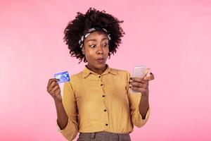 portrait de une africain américain femme permanent sur une rose Contexte en portant téléphone intelligent et argent, remise en argent. femme en portant argent et payant en ligne sur sa mobile téléphone photo