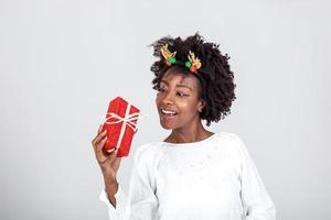 de bonne humeur bien à la recherche Jeune femme en portant une rouge Noël cadeau boîte dans sa mains, contre une blanc Contexte. concept vacances et présente photo