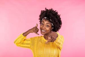 Jeune magnifique femme Faire parlant sur le Téléphone geste et montrer du doigt à toi. africain américain femme portant décontractée vêtements, souriant et à la recherche à caméra photo