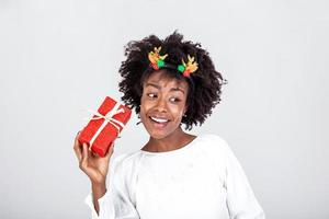 excité noir femme tremblement enveloppé cadeau boîte recevoir présente sur sa anniversaire ou Noël permanent plus de blanc Contexte. studio coup photo