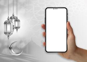 une main en portant une téléphone avec une croissant lune et une croissant lune pendaison sur le mur islamique Ramadan .téléphone intelligent maquette photo