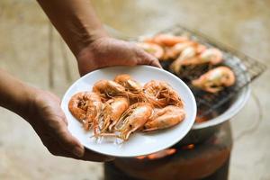 main en portant crevette grillé crevettes cuit dans le Fruit de mer restaurant - Frais crevettes servi sur assiette photo