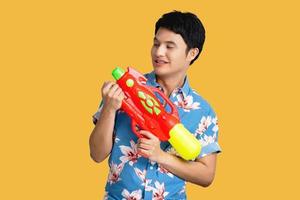 Jeune asiatique homme dans le thaïlandais Songkran festival. il détient une l'eau pistolet et porte couleurs sur une Jaune Contexte. photo