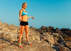 magnifique athlète femme Faire sport exercice avec le corde sur le rochers par le mer photo