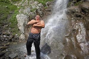 un personnes âgées homme des stands à une Montagne cascade, jouit le moment. photo