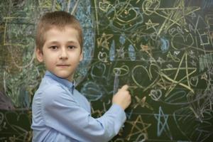 le écolier à le tableau noir dessine avec craie. milieu école âge. le garçon est dans le Salle de classe. photo