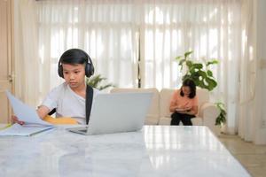 garçon asiatique jouant de la guitare et regardant un cours en ligne sur un ordinateur portable tout en s'entraînant pour apprendre de la musique ou un instrument de musique en ligne à la maison. les garçons étudient en ligne avec des professeurs d'appel vidéo jouent de la guitare. photo