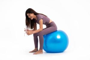 en bonne santé asiatique femme séance et boisson nettoyer l'eau sur fitball sur isolé blanc arrière-plan, concept de bien santé départs avec exercer. photo