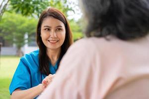 un soignant ou une infirmière asiatique prudente tient la main du patient et encourage le patient en fauteuil roulant. concept de retraite heureuse avec les soins d'un soignant et l'épargne et l'assurance maladie senior. photo