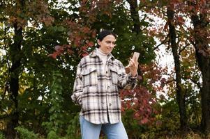 mignonne fille a une vidéo appel sur le téléphone contre le Contexte de un l'automne forêt photo