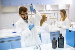 Jeunes chercheurs en vêtements de travail de protection debout dans le laboratoire et flacon d'analyse avec un liquide photo