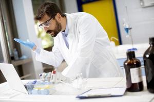 Chercheur en blouse blanche travaillant à l'aide d'un ordinateur portable alors qu'il était assis dans le laboratoire photo