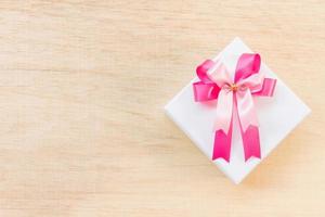 Noeud de ruban rose sur une boîte cadeau blanche sur un fond en bois