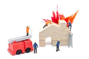 Les pompiers miniatures s'occupant d'une urgence incendie dans une maison en bois