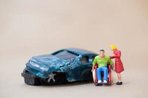 Homme handicapé miniature assis dans un fauteuil roulant sur un fond de bois, concept d'accident de voiture photo