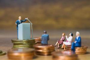 homme d'affaires miniature s'exprimant sur un podium sur une pile de pièces de monnaie, entreprise et concept d'investissement financier photo