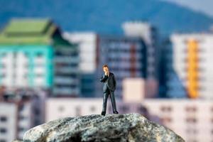 homme d'affaires miniature debout sur un rocher avec des bâtiments en arrière-plan photo