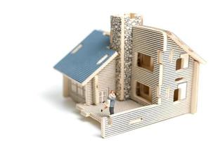 Couple miniature devant une maison en bois sur fond blanc