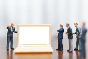 Hommes d'affaires miniatures pensant avec un projet de présentation des investissements sur un ordinateur portable à écran blanc, concept d'entreprise et technologique photo