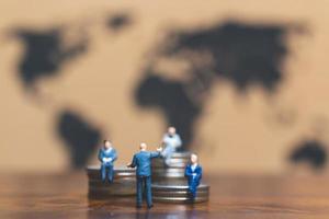 Hommes d'affaires miniatures sur une pile de pièces avec une carte du monde en arrière-plan, argent et concept de réussite commerciale financière photo
