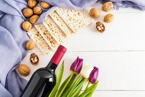 de fête Contexte pour de le juif Pâque avec matzah , noix, une bouteille de rouge du vin et fleurs. plat allonger . espace pour texte. blanc en bois planches. photo