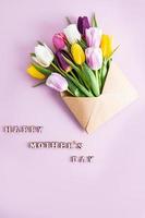 une bouquet de coloré printemps tulipes dans une artisanat enveloppe. verticale Créatif regarder. rose Contexte. le texte de une content de la mère journée. photo