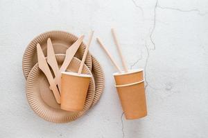 éco amical jetable papier carton vaisselle. assiettes, tasses et tuyaux, et en bois des couteaux sur une lumière Contexte. Haut voir. copie espace photo