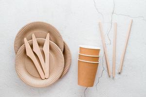 éco amical jetable papier carton vaisselle. assiettes, tasses et tuyaux, et en bois des couteaux sur une lumière Contexte. Haut voir. photo