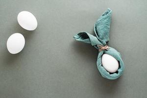 une blanc poulet Oeuf est enveloppé dans une serviette de table dans le forme de une lapin et autre des œufs sont proche sur une vert Contexte. éco amical content Pâques. Haut voir. photo