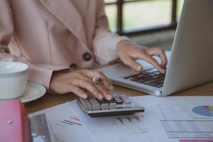 jeune femme d'affaires à l'aide d'une calculatrice travaillant sur un ordinateur portable à son poste de travail photo