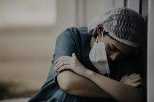 une infirmière asiatique fatiguée et déprimée porte un masque facial uniforme bleu assis sur le sol de l'hôpital, jeune femme médecin stressée par un travail acharné photo