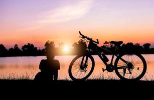 silhouette femme asseoir près vélo sur le coucher du soleil. photo