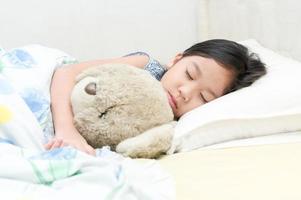 mignonne peu asiatique fille sommeil et étreinte nounours ours sur lit. photo