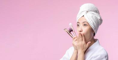 portrait content Jeune asiatique femme avec Naturel faire en haut visage en portant cosmétique peau poudre fard à joues isolé sur rose Contexte. femelle appliquer soin de la peau brosse traitement. beauté produit, cosmétologie concept. photo