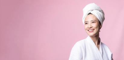magnifique Jeune asiatique femme content avec nettoyer visage peau dans serviette et peignoir de bain, spa costume sur rose Contexte. soins de la peau, traitement, bien-être thérapie, faciale se soucier, beauté femelle santé, cosmétologie concept photo