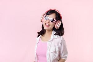 content Jeune asiatique femme modèle avec élégant branché Soleil des lunettes prendre plaisir écoute la musique par casque de musique l'audio et dansant isolé sur rose studio Contexte. technologie, fille mode, accessoire concept. photo