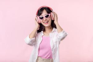 content Jeune asiatique femme modèle avec élégant branché Soleil des lunettes prendre plaisir écoute la musique par casque de musique l'audio et dansant isolé sur rose studio Contexte. technologie, fille mode, accessoire concept. photo