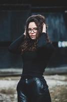 magnifique Jeune femme avec brunette frisé cheveux, portrait dans œil des lunettes profiter le Soleil dans le ville. photo